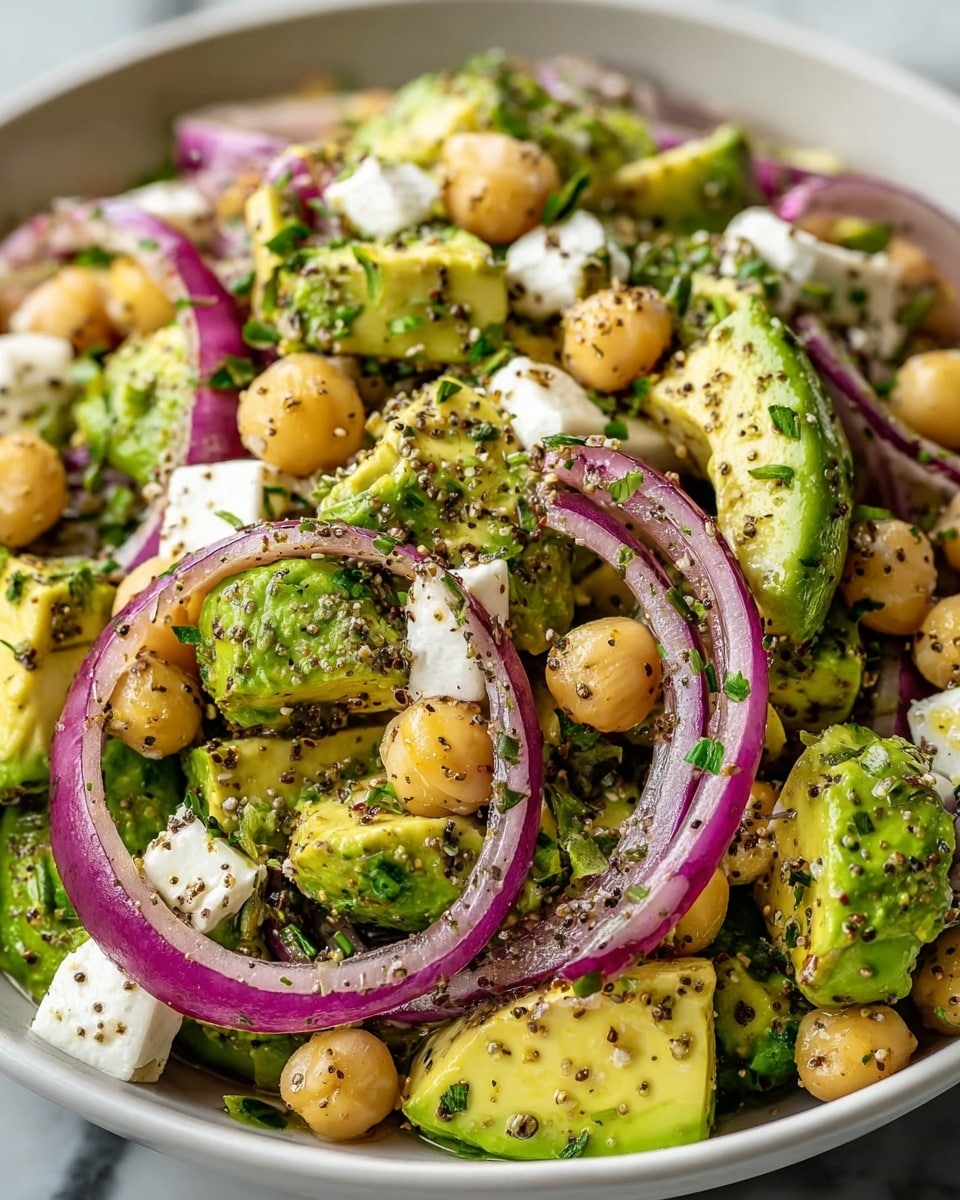 A close-up of a white bowl filled with a fresh salad made of chunky green avocado pieces, round beige chickpeas, bright purple thinly sliced onion rings, and small white cubes of cheese. The ingredients are mixed with finely chopped dark green herbs and sprinkled with coarse black pepper. The salad looks juicy and colorful on a white marbled surface. photo taken with an iphone --ar 4:5 --v 7