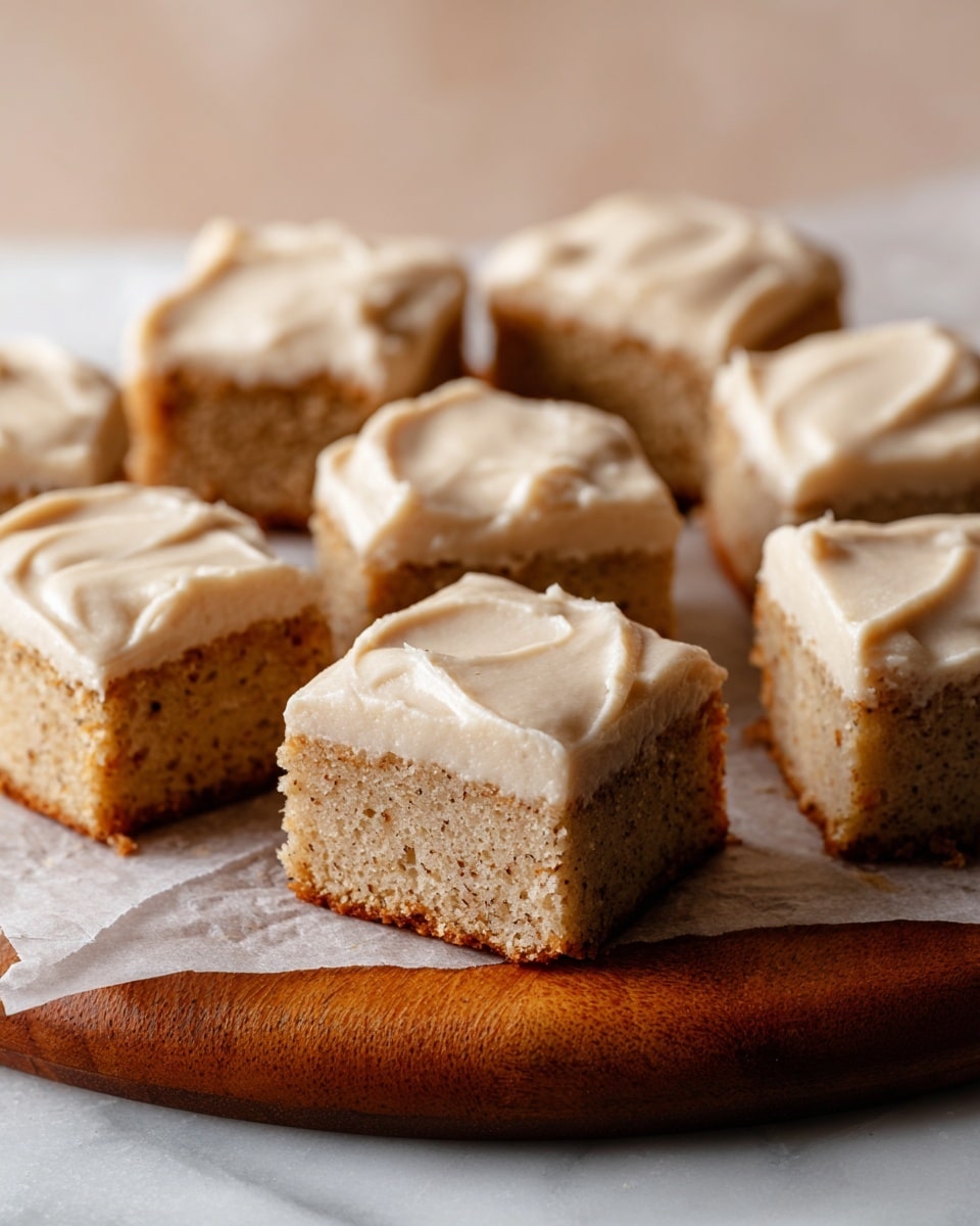 The image shows three square pieces of cake stacked close together, each cake having two layers: a thick, light brown moist base speckled with small dark bits, and a smooth, creamy off-white frosting layer on top that looks soft and slightly glossy. The cake texture is crumbly but moist with a slightly golden brown bottom edge, while the frosting layer is evenly spread with gentle swirls and soft edges. The cakes are placed on a white marbled texture surface, making the light colors of the cake and frosting stand out clearly. photo taken with an iphone --ar 4:5 --v 7