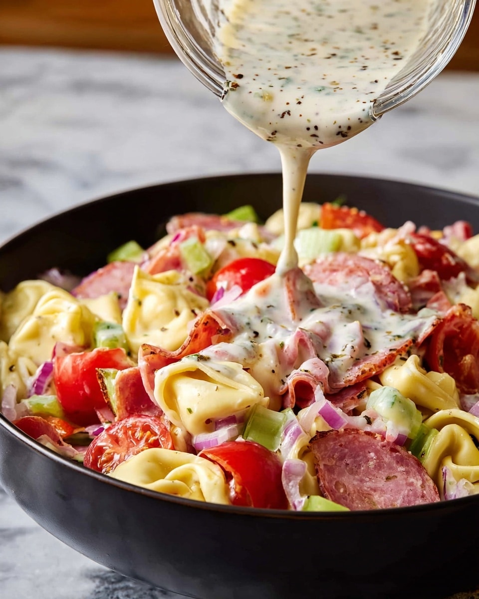 A close-up view of a black bowl filled with a colorful salad, showing layers of tortellini pasta in pale yellow, cherry tomatoes in bright red, chopped ham in light pink, pieces of salami in darker reddish-brown, small diced celery in light green, and bits of red onion in purple scattered evenly. A thick, creamy dressing with herbs and pepper is being poured from a clear glass container, creating a white layer with black specks on top of the salad. The background is a white marbled texture. photo taken with an iphone --ar 4:5 --v 7