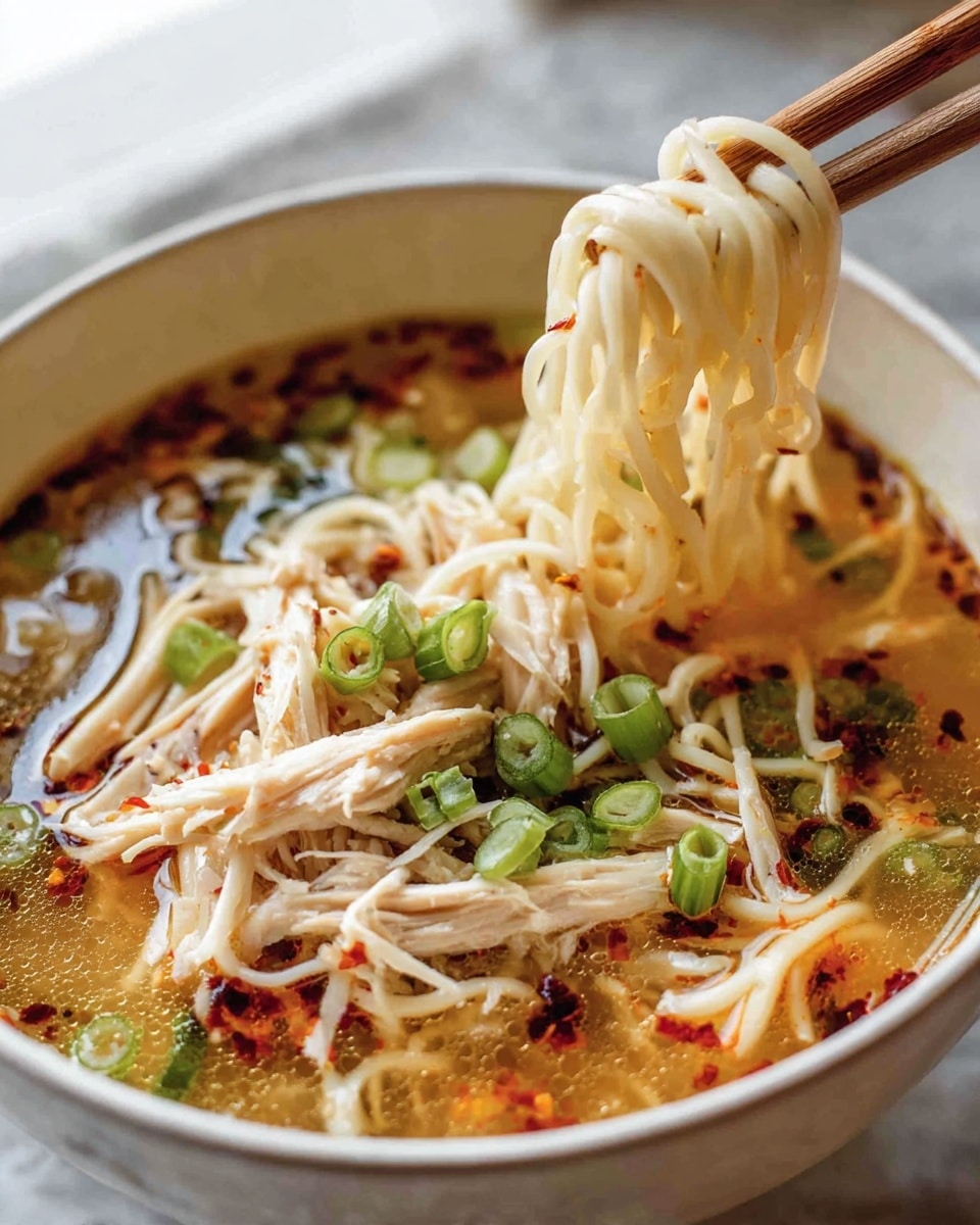 A close-up of a white bowl filled with steaming ramen soup; the bottom layer is a clear, light brown broth with oily red chili bits floating on the surface, mixed with tender shredded chicken pieces in white and light tan, thin noodles in pale yellow lifted by wooden chopsticks held by a woman's hand, and green sliced scallions scattered on top, adding bright green color. photo taken with an iphone --ar 4:5 --v 7