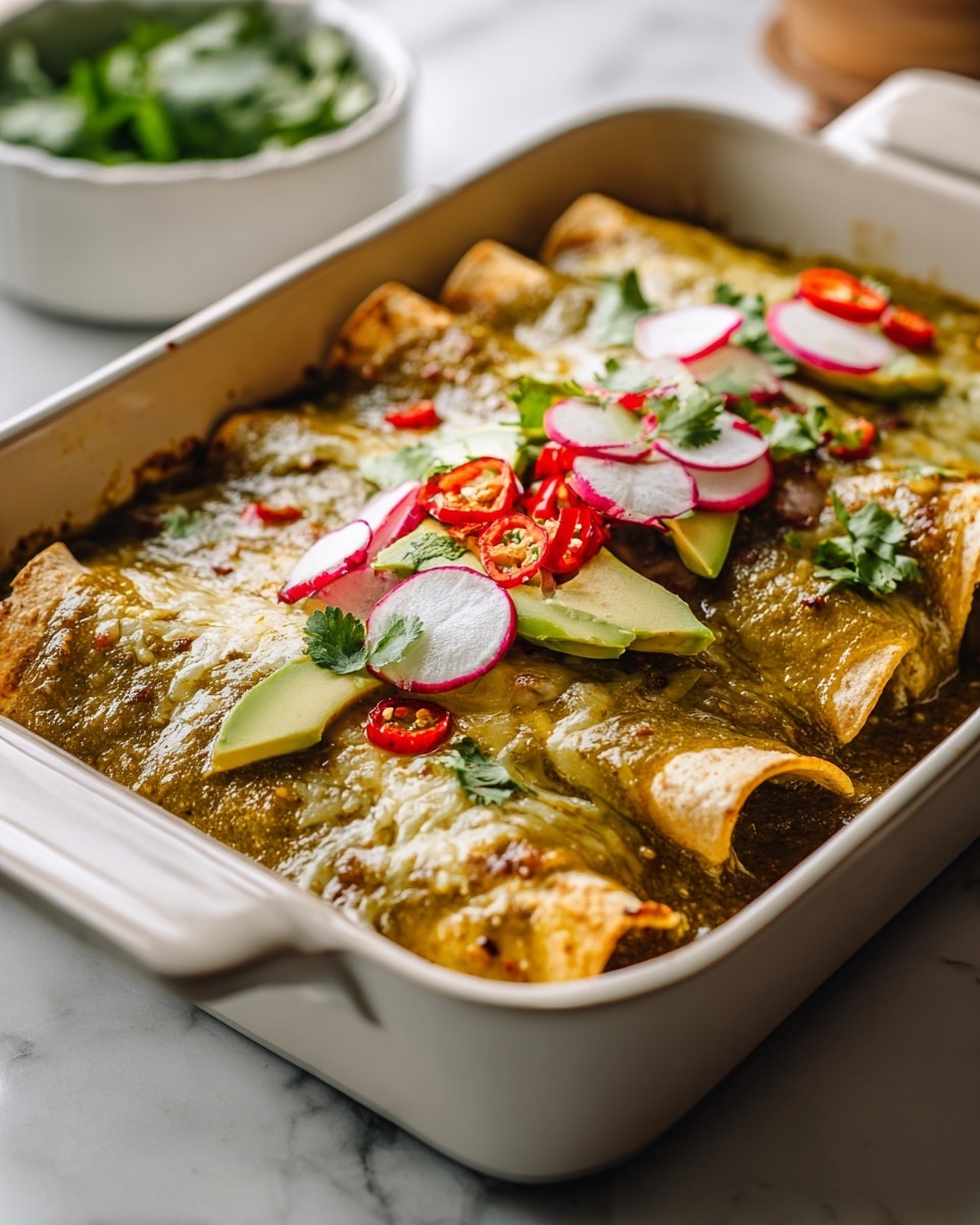 The image shows a white baking dish filled with three rolled enchiladas covered in a melted, green sauce that has a smooth and slightly chunky texture. Each enchilada has a golden brown edge where the tortilla is slightly crisp. On top of the green sauce is a colorful layer of fresh toppings including thinly sliced radishes with their white centers and pink edges, bright green cilantro leaves, small red chili pieces, and slices of light green avocado. The dish sits on a white marbled surface with a blurred white bowl containing green leaves in the background. photo taken with an iphone --ar 4:5 --v 7