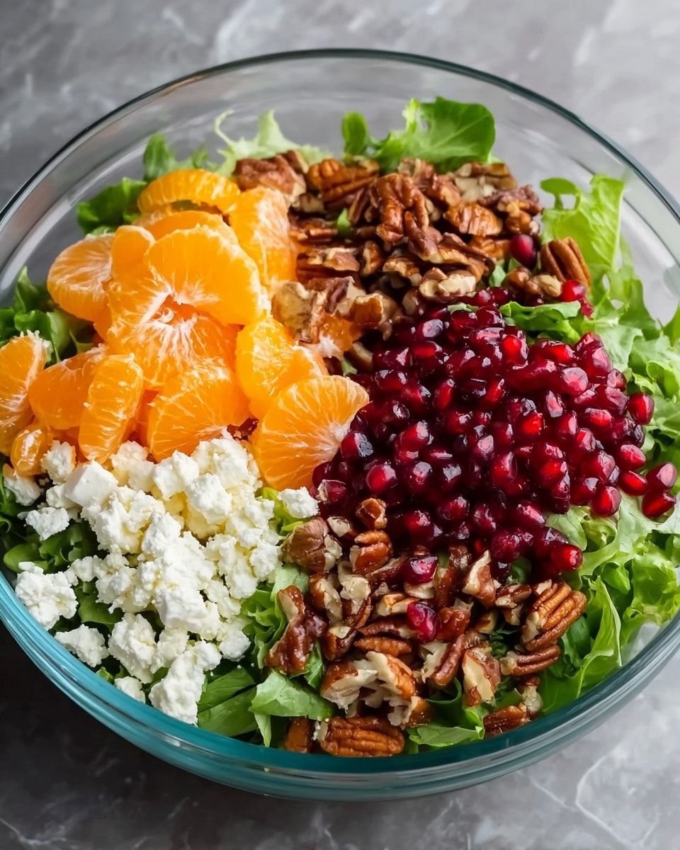 A clear glass bowl sits on a white marbled texture surface, filled with a colorful salad that has about four layers: a bed of mixed green leafy lettuce at the bottom, topped on one side with bright orange mandarin slices, on another side with white crumbly cheese, next to that a pile of crunchy brown chopped pecans, and lastly a cluster of shiny red pomegranate seeds. The colors and textures create a fresh and vibrant look. photo taken with an iphone --ar 4:5 --v 7