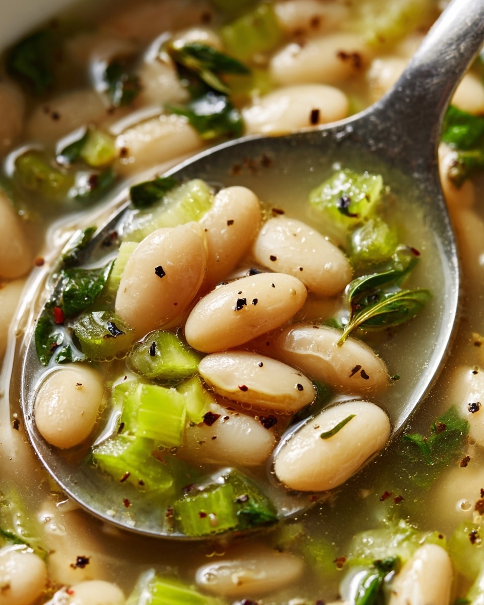 A close-up image of a spoon filled with cooked white beans in a clear broth, with small green herb pieces and light green chopped celery evenly mixed throughout; the beans are plump and shiny with a smooth texture, and the broth looks slightly oily with visible black pepper specks. The background shows more of the same mixture, sitting on a white marbled surface. Photo taken with an iphone --ar 4:5 --v 7