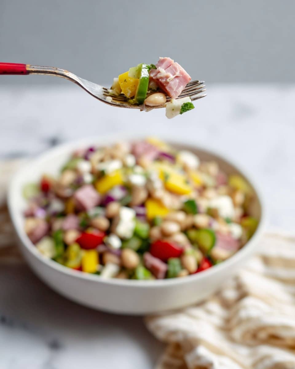 A close-up of a fork with a silver handle and a red tip holding a small mix of layered salad ingredients: pale beans at the base, pieces of pink ham, white cheese cubes, bright yellow pepper rings, chopped red onions, and green herbs. Below, there is a white bowl filled with a colorful mix of the same ingredients, showing more yellow peppers, red tomatoes, green onions, and white beans. The bowl sits on a white marbled surface with a striped cloth beside it. The background is a soft light gray. Photo taken with an iphone --ar 4:5 --v 7
