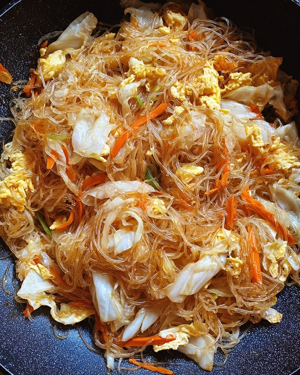 A pan filled with cooked clear glass noodles mixed with chopped white cabbage pieces that have a smooth and soft texture, thin orange carrot strips, and scrambled egg chunks that are yellow and fluffy. The noodles are slightly glossy and tangled throughout the dish, blending with the vegetables and egg. The pan has a dark and textured surface underneath the mix of ingredients. photo taken with an iphone --ar 4:5 --v 7