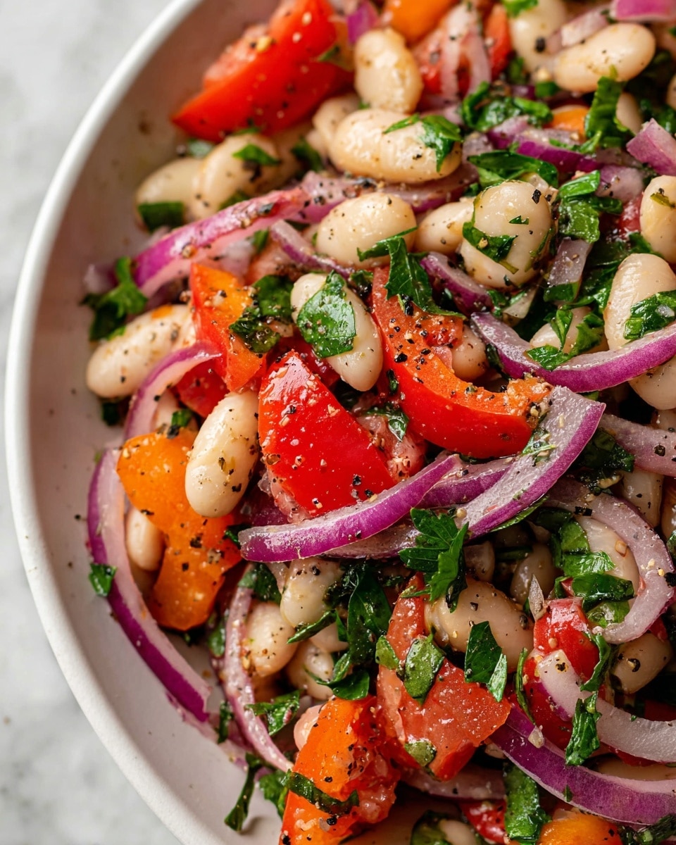 A close-up view of a colorful salad showing mixed layers of white beans, bright red and orange chunks of bell peppers, and thinly sliced purple onion rings scattered throughout. Fresh green parsley leaves are mixed in, adding a bright and leafy texture. The ingredients are coated with a light dressing sprinkled with black pepper, giving a slightly shiny and seasoned look. The entire salad sits on a white marbled surface. photo taken with an iphone --ar 4:5 --v 7