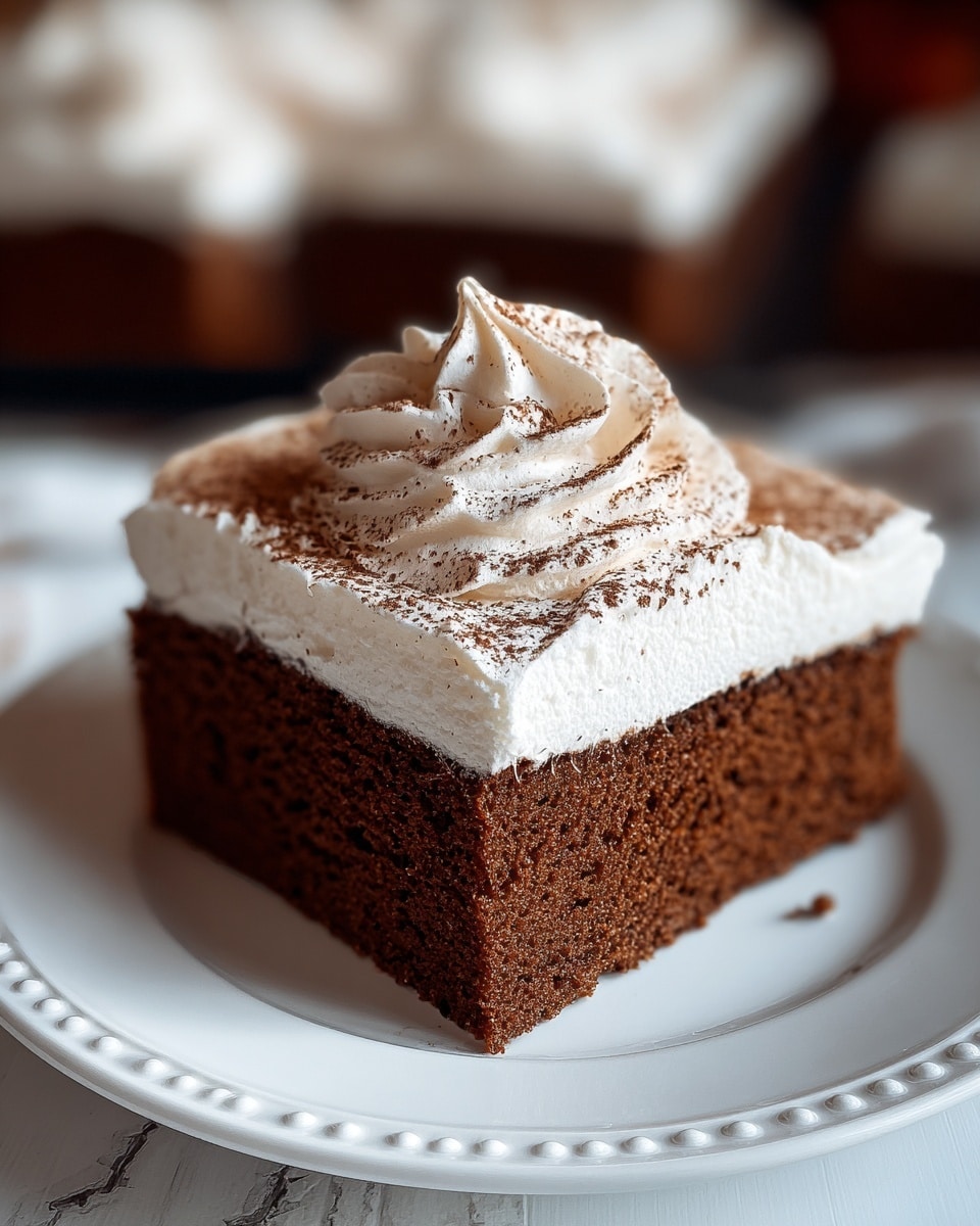 A single square piece of chocolate cake with a dense, moist texture forms the bottom layer in rich brown. On top, there is a thick, smooth layer of white whipped cream frosting, spread evenly and finished with a small swirl peak in the center. The whipped cream is sprinkled lightly with cocoa powder, adding a dark brown dusting on top. The cake sits on a white plate with a beaded edge design. The background is a white marbled texture, slightly blurred with other similar cake pieces visible. photo taken with an iphone --ar 4:5 --v 7