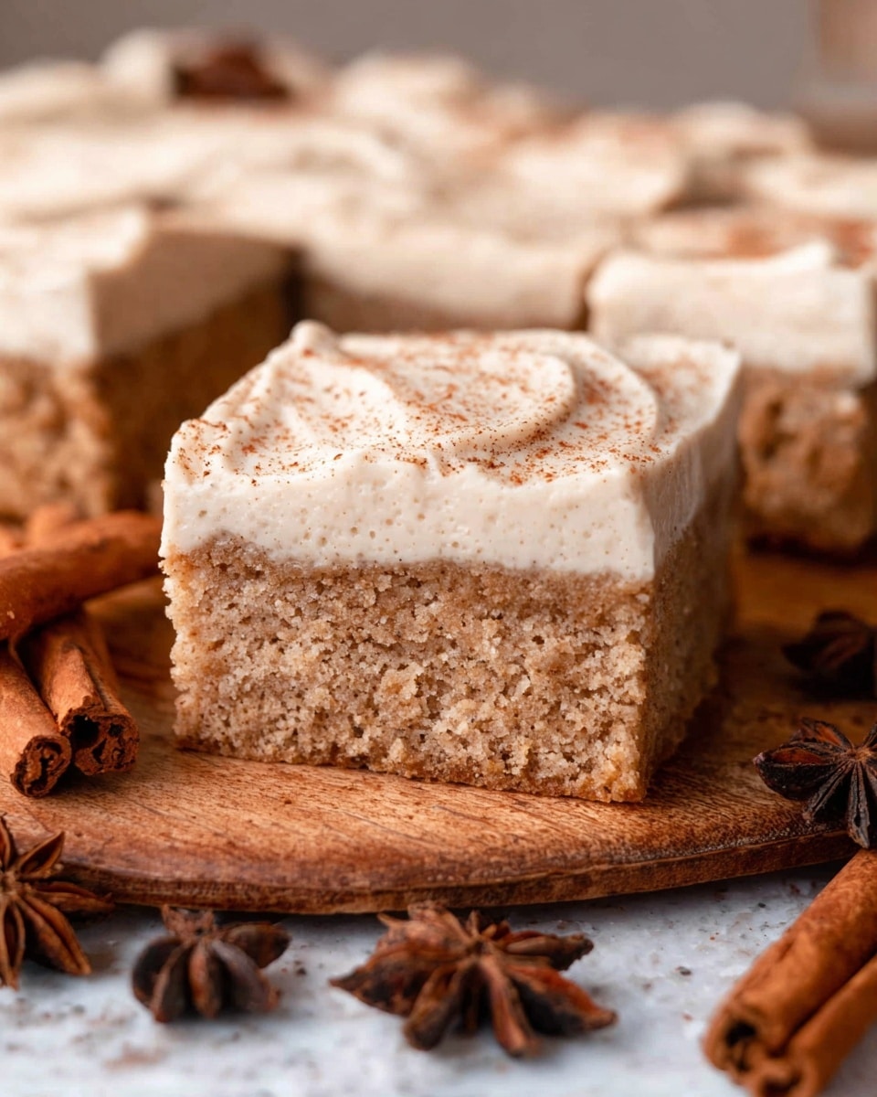 This image shows a square piece of spice cake with two distinct layers: a thick, light brown, moist and crumbly bottom layer topped with a creamy, light beige frosting layer sprinkled lightly with cinnamon powder. The cake piece is cut neatly from a larger cake of the same, with more pieces served in the background on a wooden surface. Nearby are whole cinnamon sticks and star anise spices as decorations, all set on a white marbled textured surface. Photo taken with an iphone --ar 4:5 --v 7