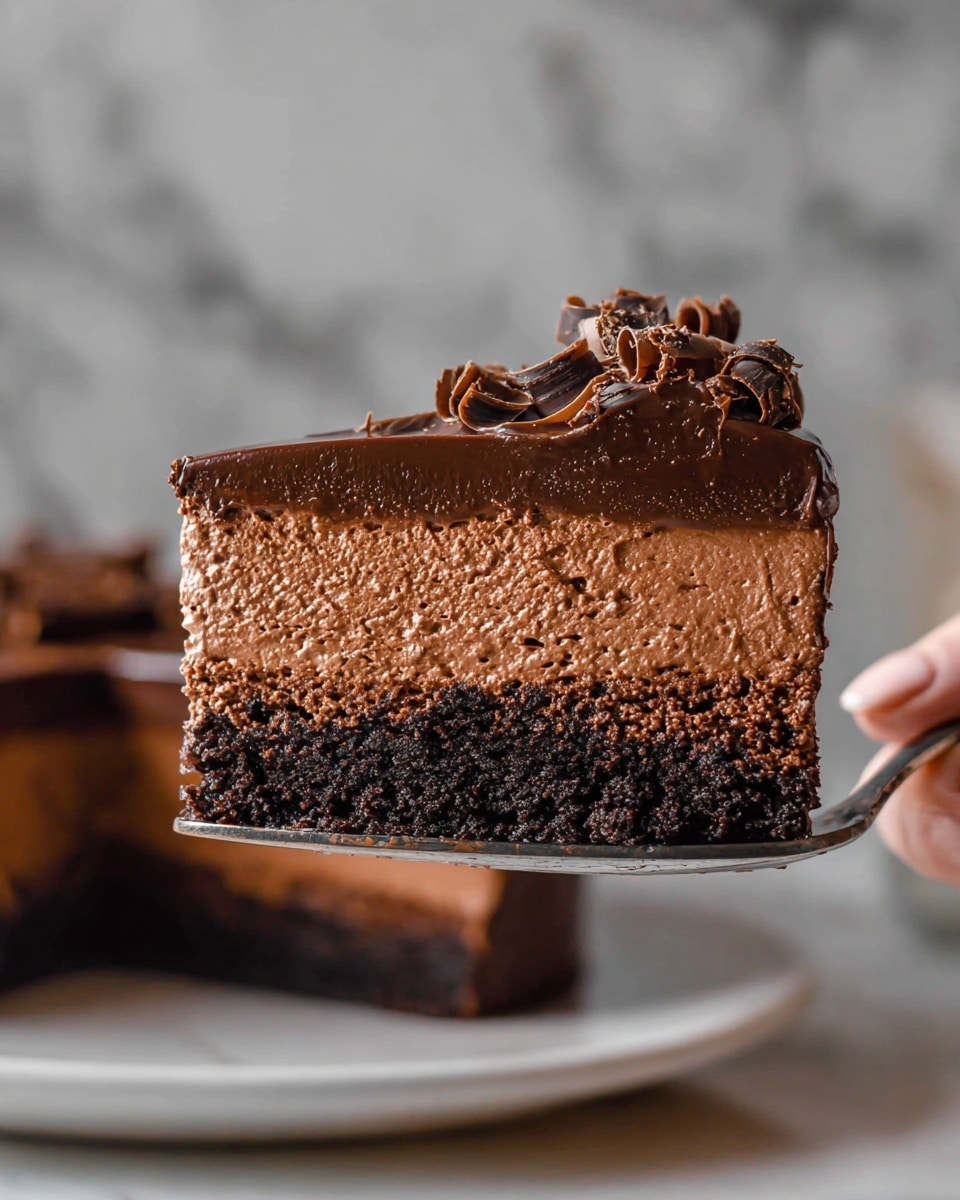 A slice of rich chocolate cake is held above a white plate with a woman's hand, showing four layers: a dark, crumbly chocolate base at the bottom, a thick layer of smooth chocolate mousse in the middle, a slightly denser chocolate layer above it, and a glossy dark chocolate ganache topping with curled chocolate shavings on top; the cake slice has a moist, creamy texture with dark and lighter brown tones and is set against a softly blurred background with a white marbled surface. photo taken with an iphone --ar 4:5 --v 7