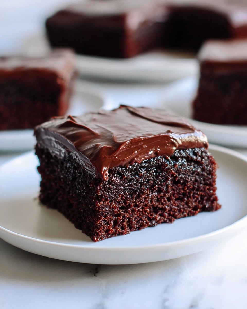 A single square piece of chocolate cake sits on a white plate, showing two clear layers: a thick, moist dark brown cake base with a light, crumbly texture and a smooth, glossy dark chocolate frosting layer on top that is thick and shiny with slight ridges made by spreading. In the background, there are more pieces of the same chocolate cake blurred out on white plates, all placed on a white marbled surface. The scene has soft natural lighting highlighting the moistness of the cake and the shine of the frosting. photo taken with an iphone --ar 4:5 --v 7